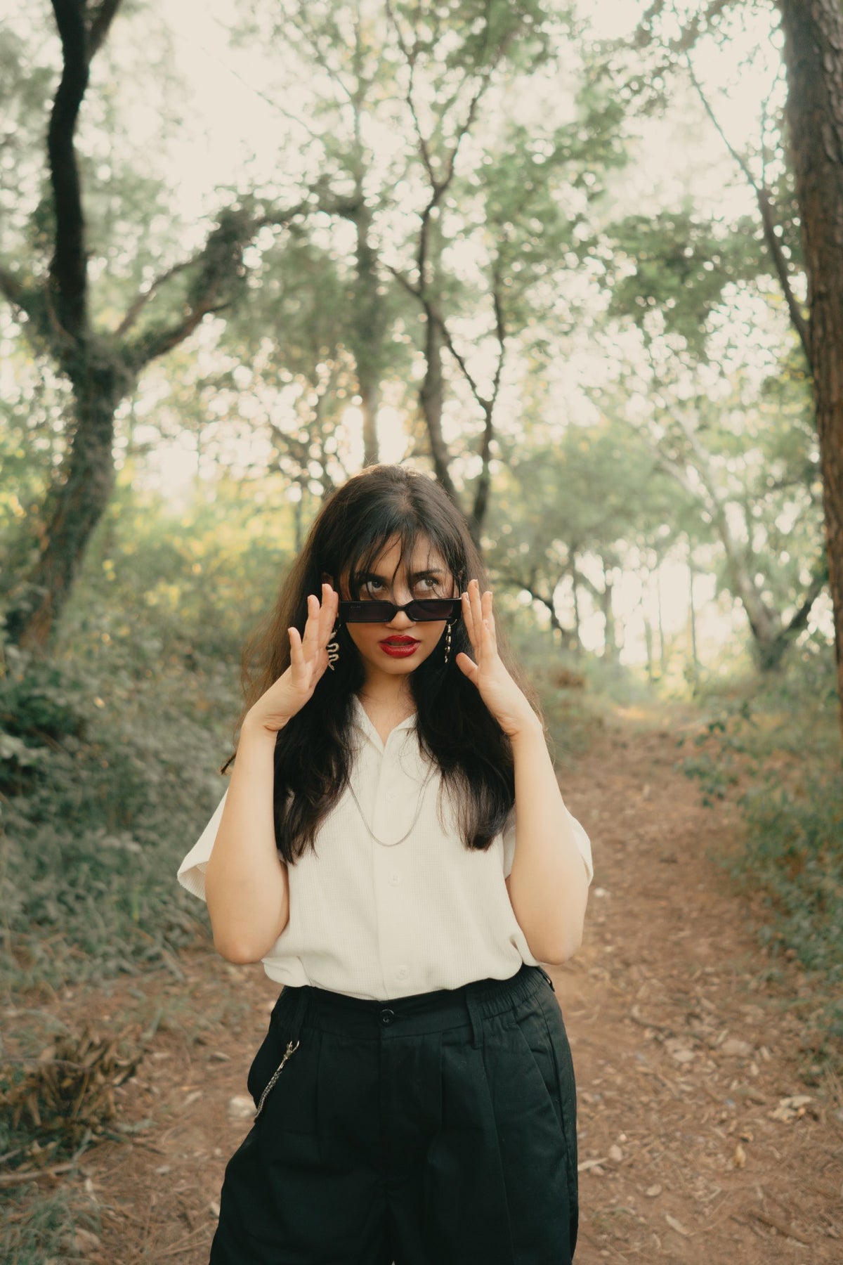 Model in the off-white Cuban collar lowering her sunglasses on a forest path